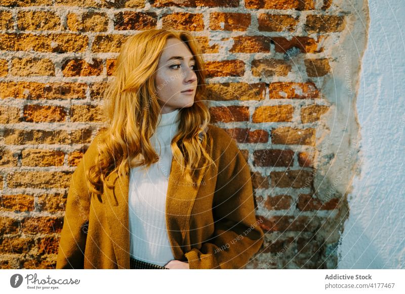 Young red haired woman in coat on street redhead appearance charming long hair brick wall style outfit female building city relax autumn ginger urban carefree