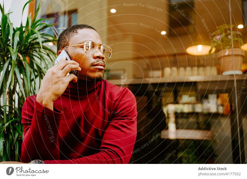 Black man talking on smartphone near cafe in city browsing surfing social media street style trendy male ethnic black african american internet mobile phone