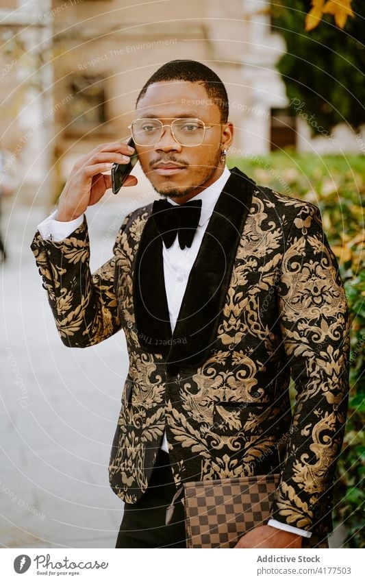 Black man in stylish suit talking mobile phone in city posh tuxedo rich outfit luxury smartphone male ethnic black african american street gadget device guy