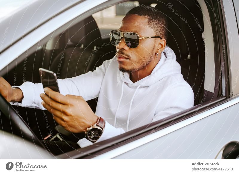 Stylish black man using smartphone in luxury car browsing posh determine surfing internet driver male ethnic african american parked modern connection transport