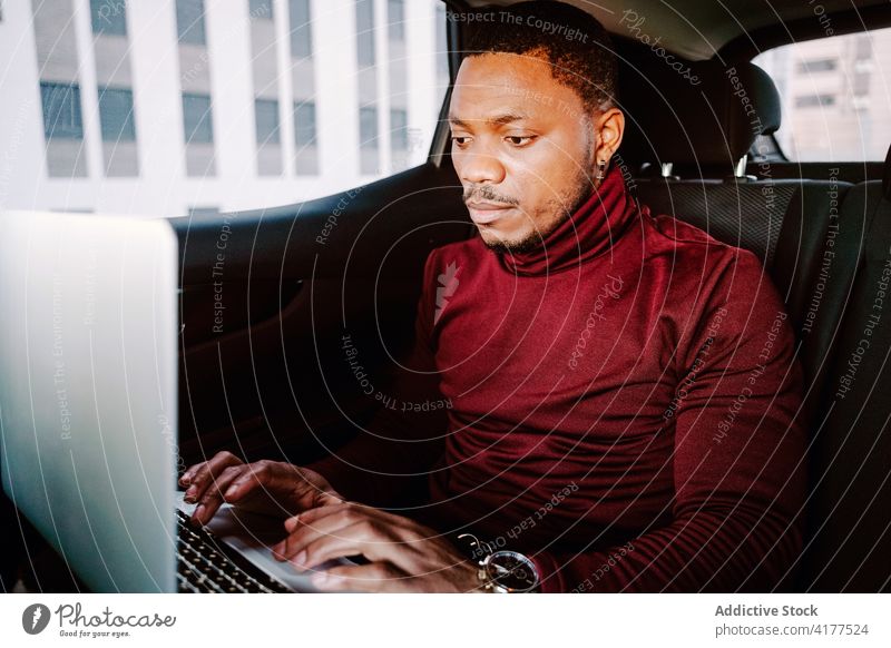 Serious black businessman typing on laptop in car work project entrepreneur busy automobile male african american ethnic backseat netbook browsing connection