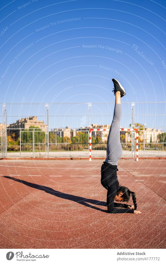 Athletic woman performing handstand on sports ground exercise balance training calisthenics acrobatic gymnastic slender athlete female sportswear wellbeing