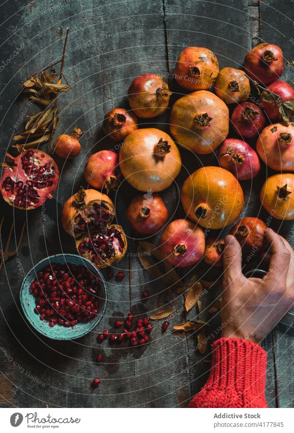 Crop anonymous person arranging ripe pomegranates on table arrange fruit pile harvest delicious rustic dark room vitamin food raw heap natural healthy organic