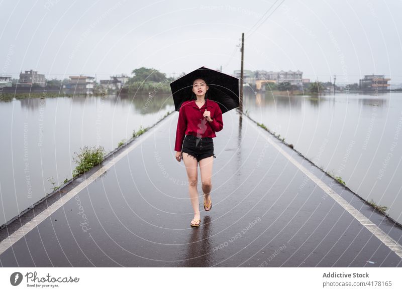 Woman walking along wet road on rainy day woman umbrella cloudy asphalt alone solitude stroll female yilan county taiwan empty overcast sky weather roadway