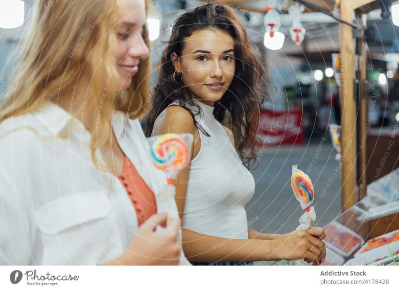 Happy girlfriends with lollipops on funfair summer happy young candy fairground enjoy holiday women teen together lifestyle cheerful teenage millennial weekend