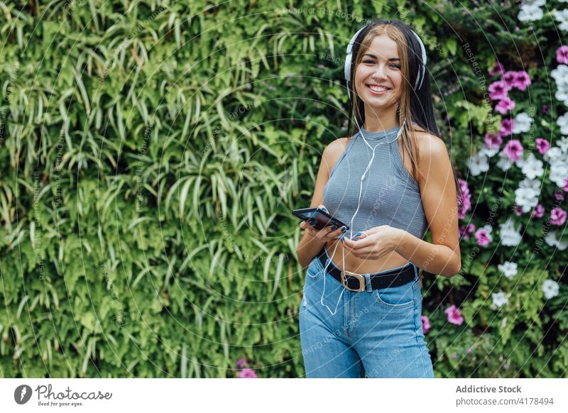 Happy woman with smartphone and headphones chilling in park happy listen having fun cheerful summer mobile music positive young female gadget device lifestyle
