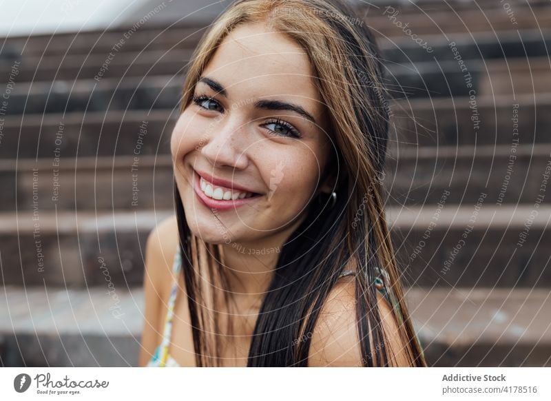 Joyful young woman resting on steps in city cheerful smile positive happy modern urban portrait long hair female brunette dyed hair millennial optimist stair