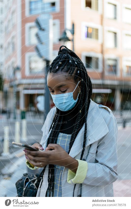 Black woman in mask using smartphone on city street coronavirus urban mobile pandemic modern young female african american black ethnic covid 19 covid19 gadget