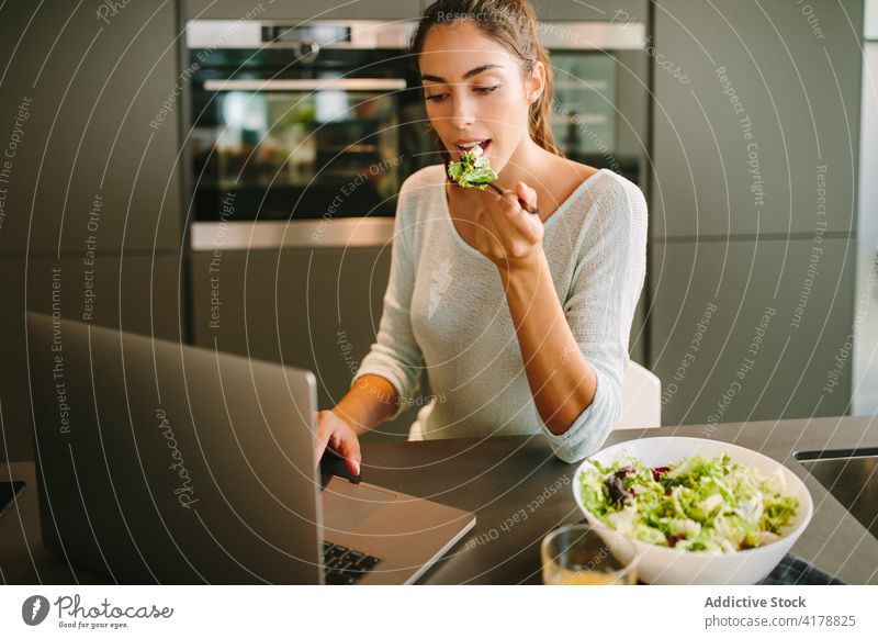 Woman eating salad and working on laptop in kitchen woman freelance lunch home remote entrepreneur female project beverage fresh refreshment gadget internet
