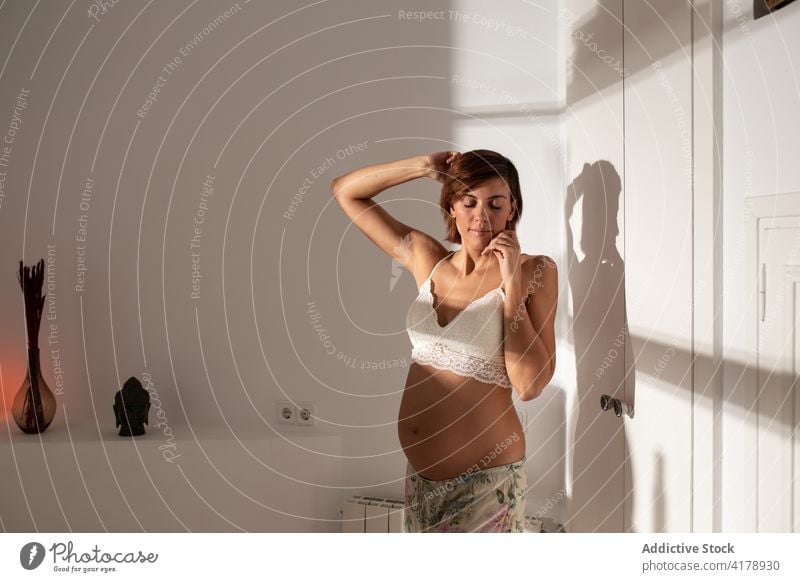 Pregnant woman stretching in room in morning awake pregnant arms raised enjoy belly pregnancy sunlight female expect carefree maternal happy bra lit relax
