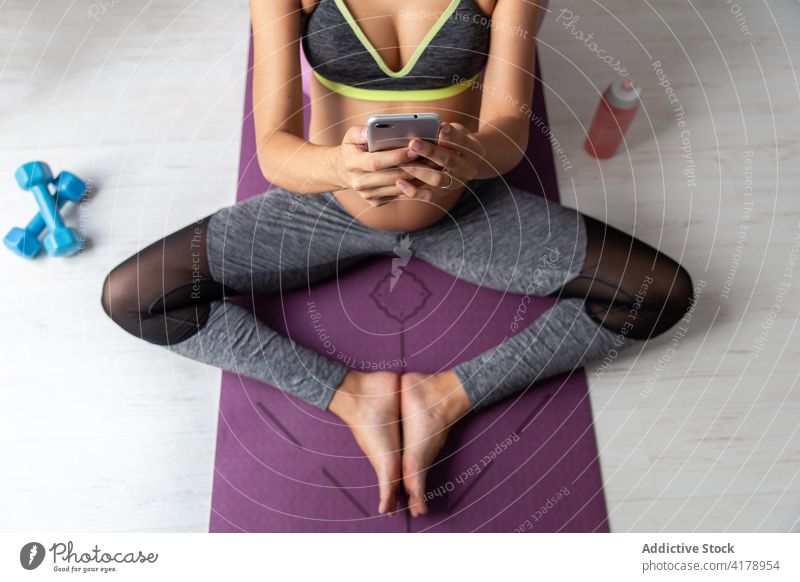 Pregnant woman on mobile phone while resting from yoga pregnant meditate relax tranquil pose female sportswear mat harmony wellbeing practice healthy asana calm