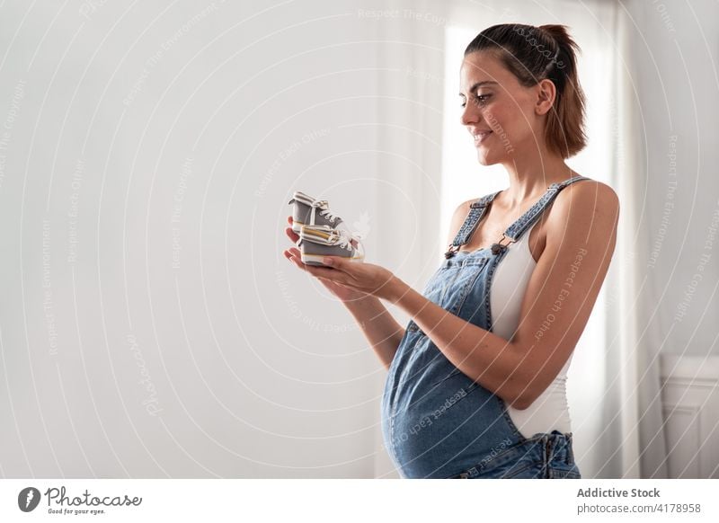 Pregnant woman standing with tiny baby boots pregnant shoe gumshoe belly pregnancy wardrobe home female small maternal expect overalls footwear motherhood