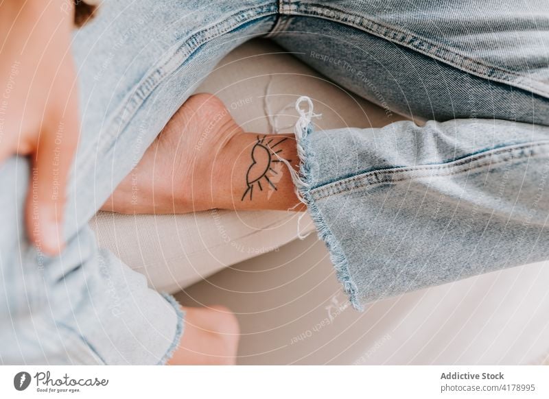 Crop woman with tattoo on leg creative sun shape art design young individuality female culture fashion cool personality sit jeans sofa rest style lady body art
