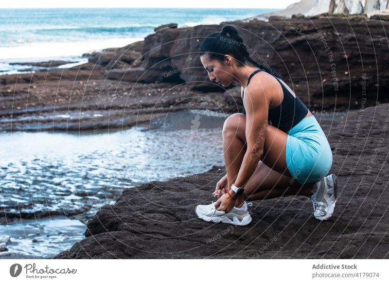 Young sportswoman tying shoelaces before training tie sneakers footwear workout prepare seashore seaside female ethnic sportswear athlete activewear healthy