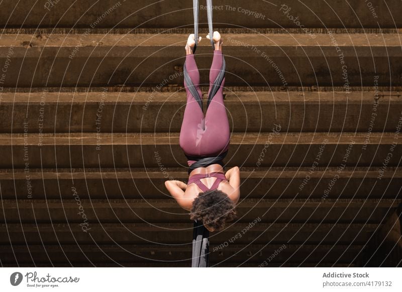Slim woman doing aerial yoga in city split pose practice silk flexible balance strap female ethnic black background african american stretch asana wellness
