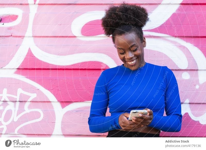 Content black woman browsing smartphone in city watching graffiti wall street art cheerful female ethnic african american afro hairstyle gadget device news