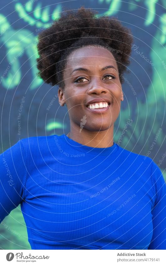Black woman standing near wall with graffiti city lean relax urban cool street art smile female ethnic black african american colorful creative curly hair happy