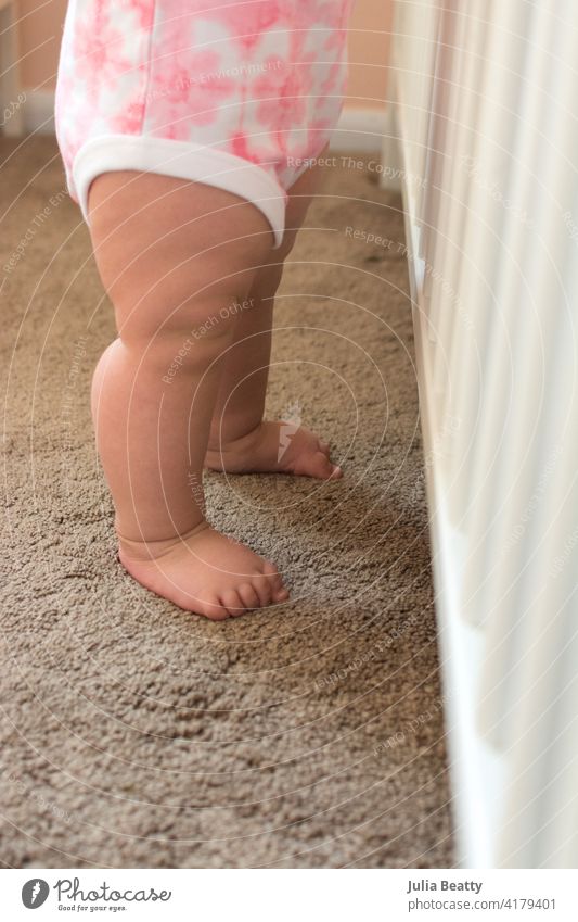Ten month old toddler holding onto crib rails and standing upright; sturdy baby legs learning walk step balance child milestone developmental cruising cruise