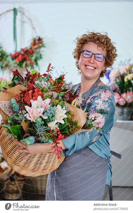 Delighted woman with bunch of flowers in shop florist basket arrangement various smile floristry apron female retail store bouquet blossom cheerful bloom owner