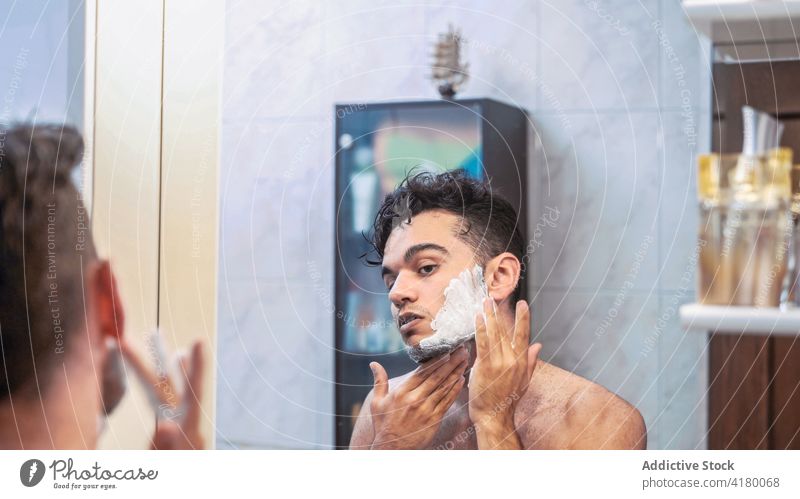 Man shaving beard in bathroom man shave razor foam routine grooming morning young male ethnic brunet mirror shirtless care manual lifestyle skin care reflection