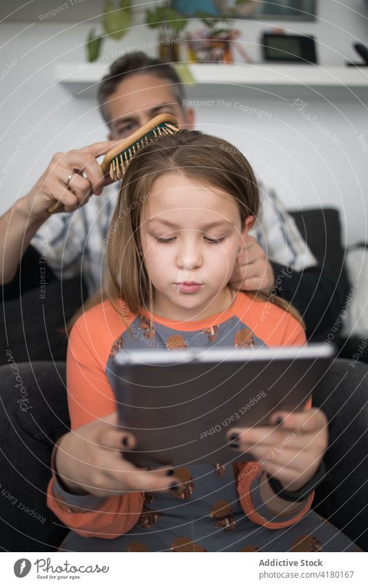 Father combing hair of daughter father brush care love kid careful child dad tablet using together parent relationship lifestyle bonding browsing gadget device