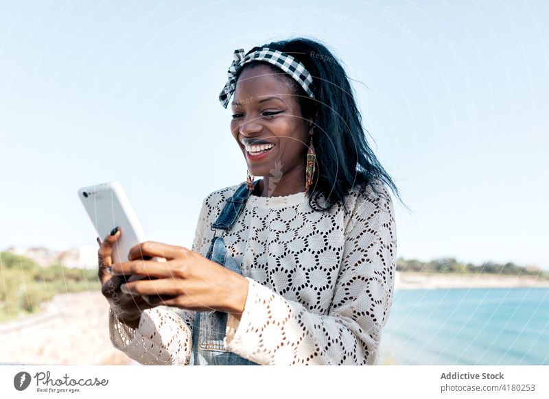 Happy black woman using smartphone on beach happy cheerful browsing mobile young gadget device lifestyle ethnic female african american smile online surfing