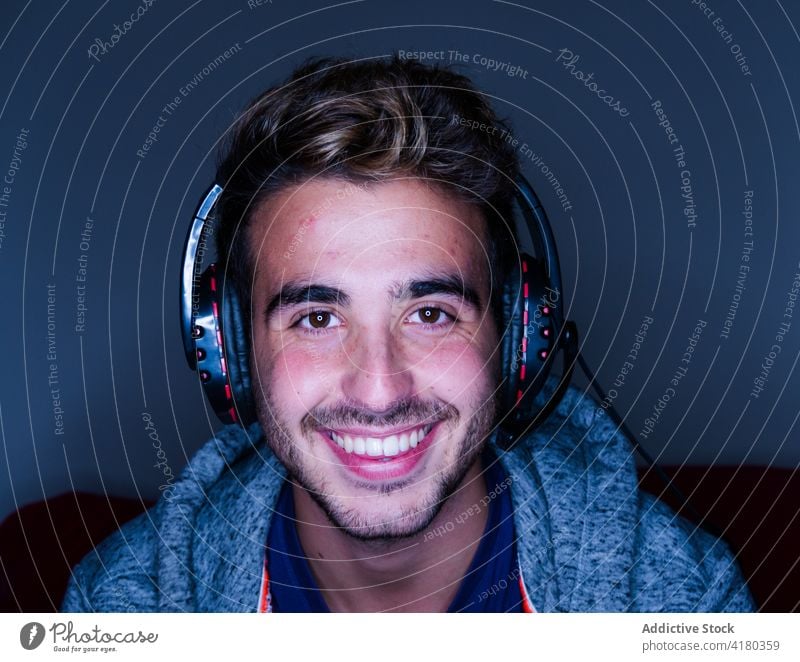 Cheerful man in headset sitting at desk with computer happy toothy smile lean on cheerful headphones work gadget dark using handsome casual wireless device