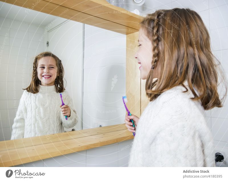 Cheerful girl brushing teeth and looking in mirror bathroom toothbrush toothy smile happy joy cheerful hygiene routine daily positive modern adorable cute young