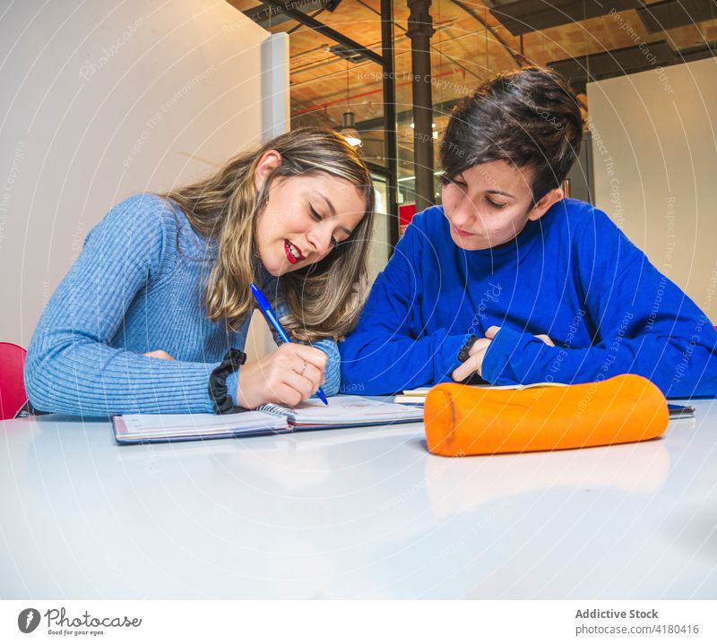 Student explaining task to classmate in classroom women student homework discuss exam preparation positive support study female information assignment together