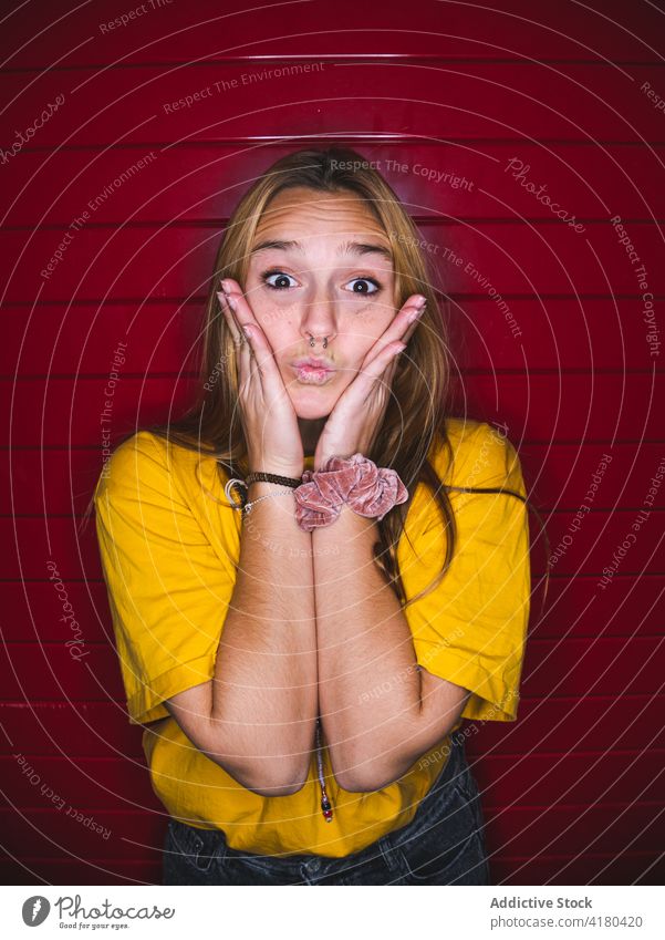 Young female doing grimace gesture while standing against red striped background woman funny coquette humor playful childish personality demonstrate make face