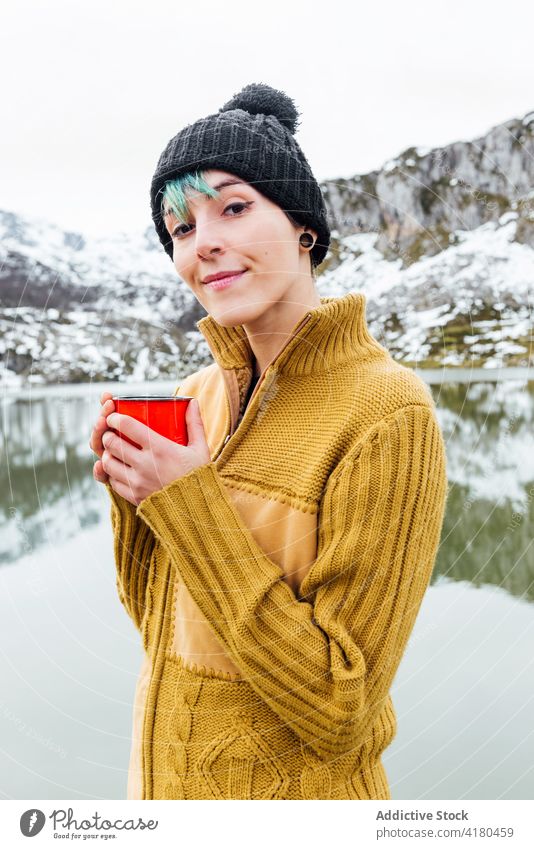 Serene woman enjoying hot drink near lake on mountainous terrain serene peaceful winter highland traveler content lakeside rocky snow asturias adventure season