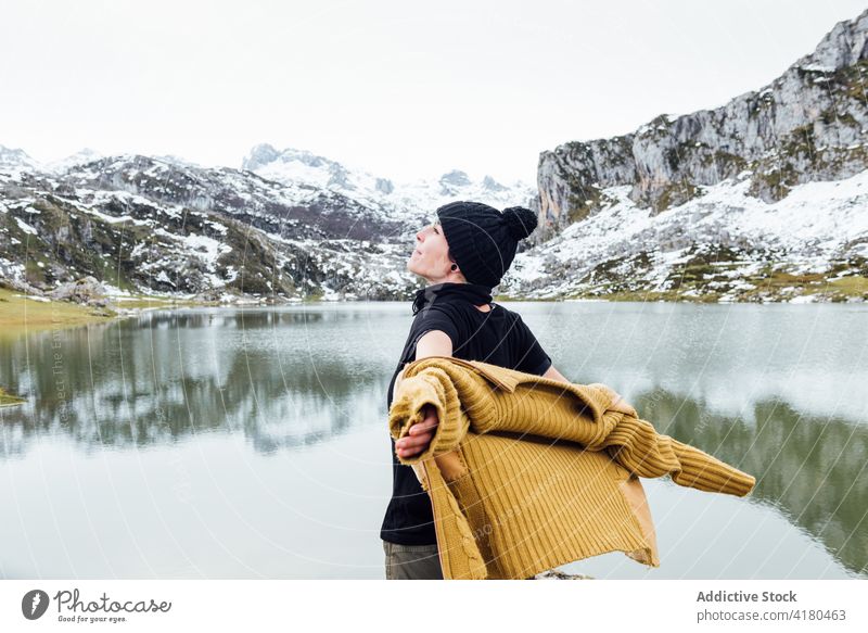 Happy woman standing with arms outstretched on cold lake shore mountain freedom joy highland traveler excited enjoy rocky lakeside winter snow asturias season