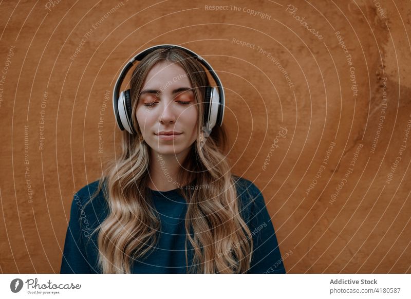 Dreamy woman listening to music in headphones in town song eyes closed thoughtful enjoy dreamy wireless using gadget street device headset modern style melody