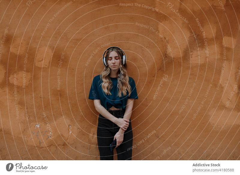 Dreamy woman listening to music in headphones in town song eyes closed thoughtful enjoy dreamy wireless using gadget street device headset modern style melody