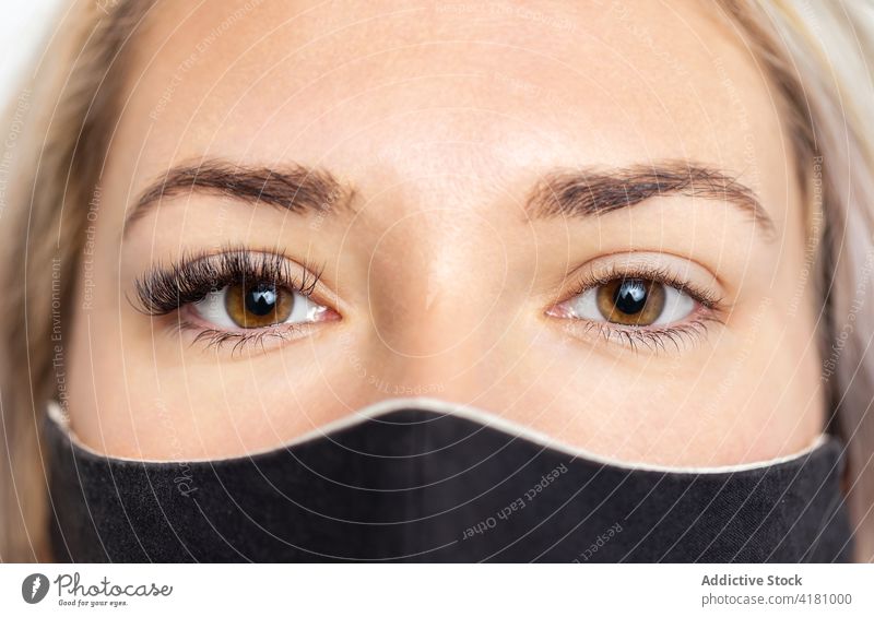 Crop woman in mask with lashes extensions on one eye eyelashes artificial cosmetology calm beauty coronavirus brown eyes glance procedure new normal cosmetic