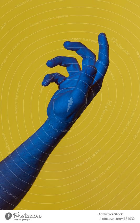 Man's blue hand holdings something invisible man dark blue over yellow background open palm pop art showing concepts isolated copyspace male person fingers