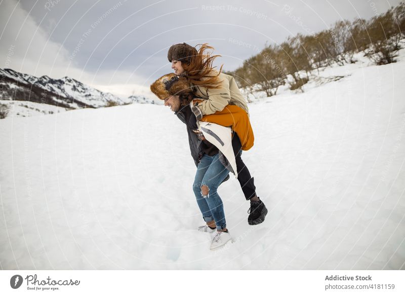 Happy woman riding piggyback on boyfriend during winter trip ride girlfriend freedom having fun snow mount nature couple lean forward carry relationship love
