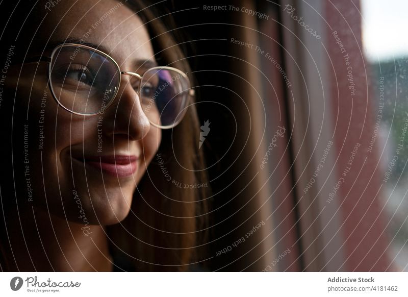 Crop smiling woman in eyeglasses looking out window smile content positive satisfied glad cheerful young enjoy dark optimist happy attractive beautiful eyewear