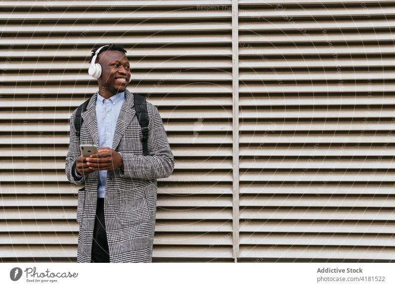 Happy black office worker chatting on smartphone near wall man text messaging bike smile internet headset city using gadget listen music watching headphones