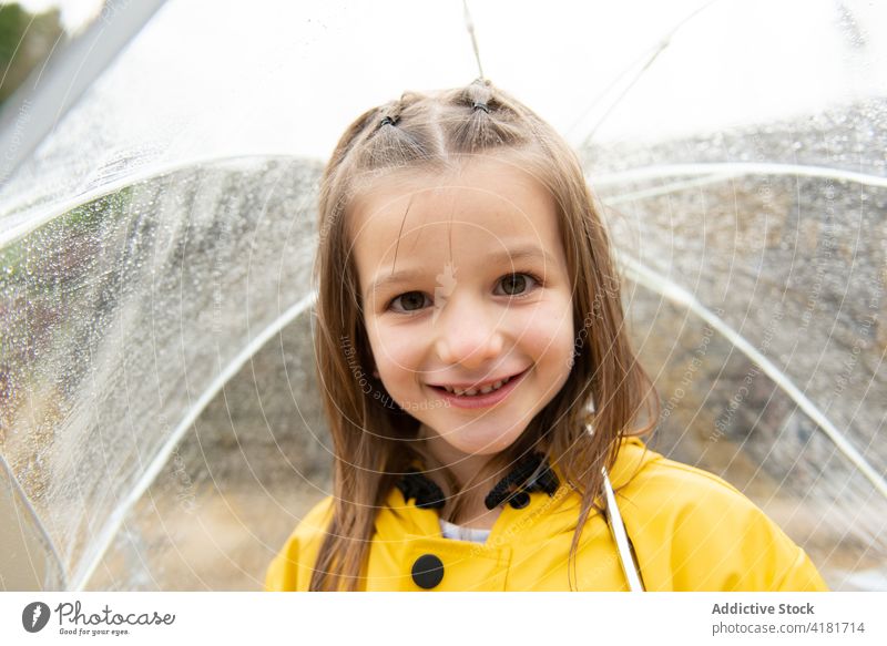 Smiling girl under umbrella on rainy day child raincoat cheerful wet waterdrop smile yellow kid transparent childhood weather charming pleasure bright autumn