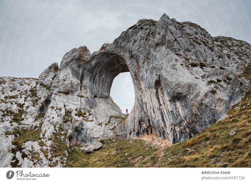 Distant traveler standing in natural rock arch hole explore mountain formation cloudy wanderlust nature asturias spain adventure overcast geology scenic trip
