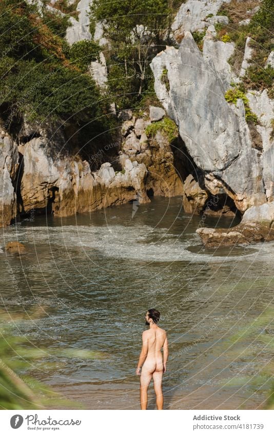 Unrecognizable naked man standing on lakeside in rocky highlands beach rough nudism cliff undress pond nude scenic nature asturias spain shore coastline bare