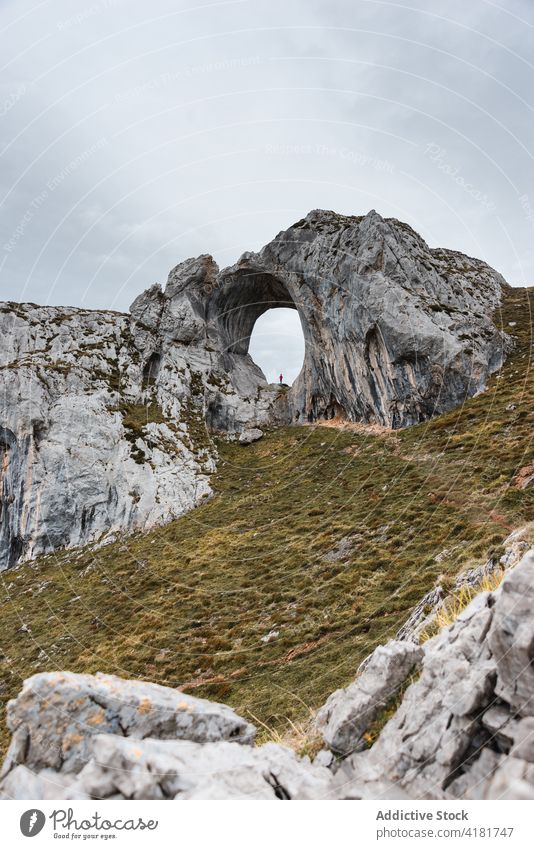 Distant traveler standing in natural rock arch hole explore mountain formation cloudy wanderlust nature asturias spain adventure overcast geology scenic trip