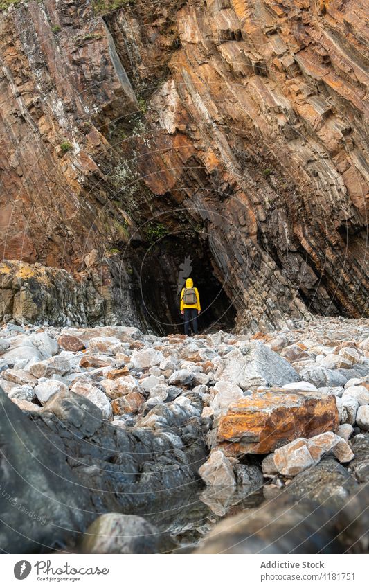 Unrecognizable traveler standing near rock cave person rough grotto stiff mountain stone formation terrain highland cliff scenic uneven environment daylight