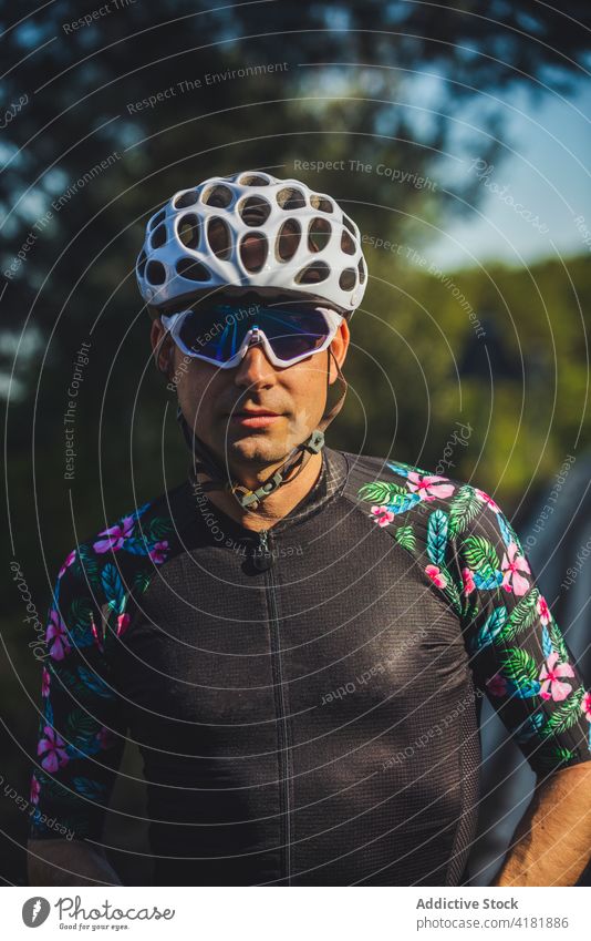 Serious sportsman in cyclist outfit standing near green trees in sunlight confident athlete park training portrait serious activity workout wellness healthy