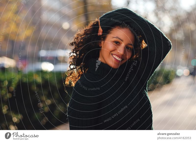 Woman smiling while posing outdoors. young woman urban street sombrero style city closeup curly hair hairstyle clothing trendy one pose confident casual