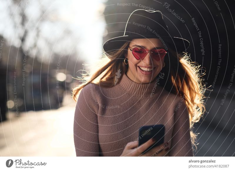 Young woman using her mobile phone outdoors. urban smartphone social media sombrero communication female sunglasses cellphone confident chat device city street