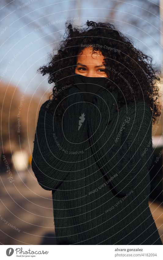 Woman with face mask while standing outdoors. woman urban street covid-19 sombrero style city closeup curly hair warm clothing pandemic new normal protective