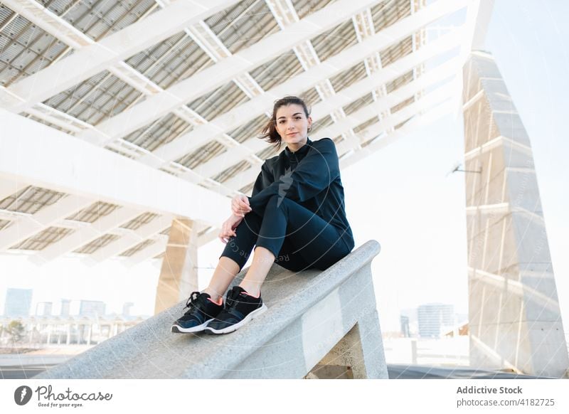 Young woman resting on concrete construction in suburb sit dreamy activewear contemplate break young slim lifestyle creative sunny slender modern sportswear