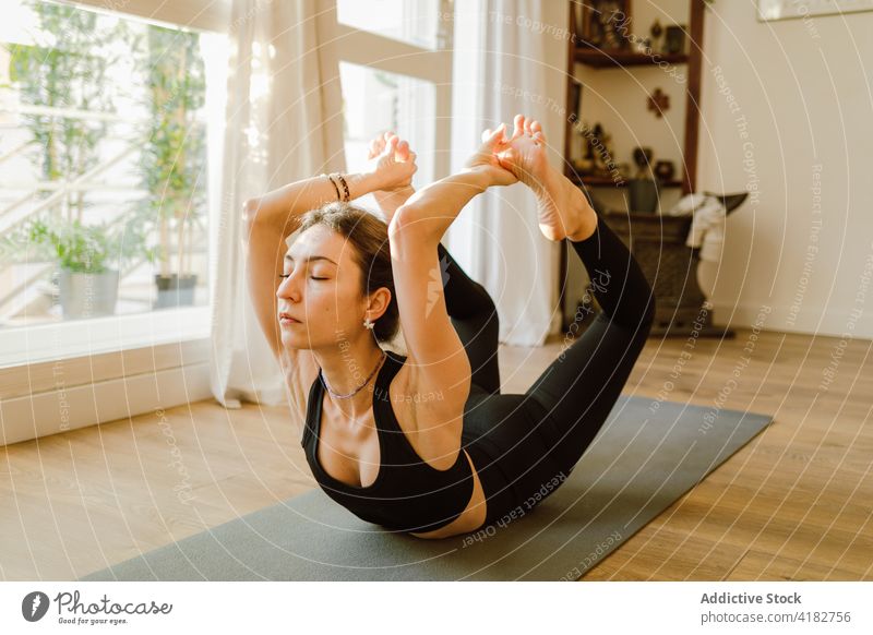 Flexible woman performing Bow pose on mat in house yoga bow pose flexible stretch practice eyes closed healthy lifestyle vitality mindfulness perfect barefoot